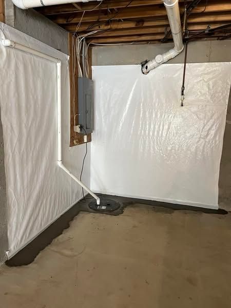Basement interior with white plastic wall covering, electrical panel, sump pump, and exposed beams.