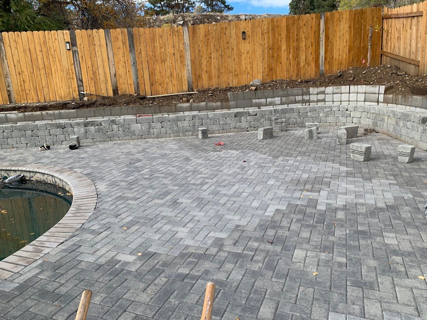 A brick patio is being built in front of a wooden fence.
