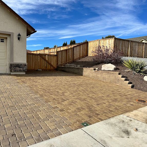 A brick driveway leading to a house with a wooden fence