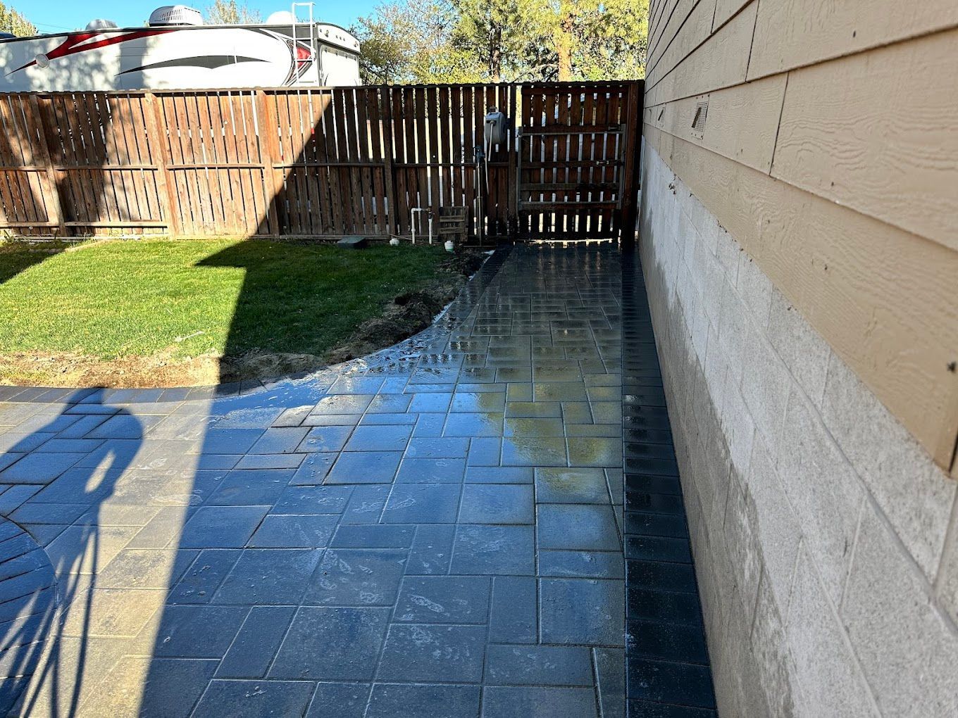 A brick walkway leading to a fenced in yard with a rv in the background.