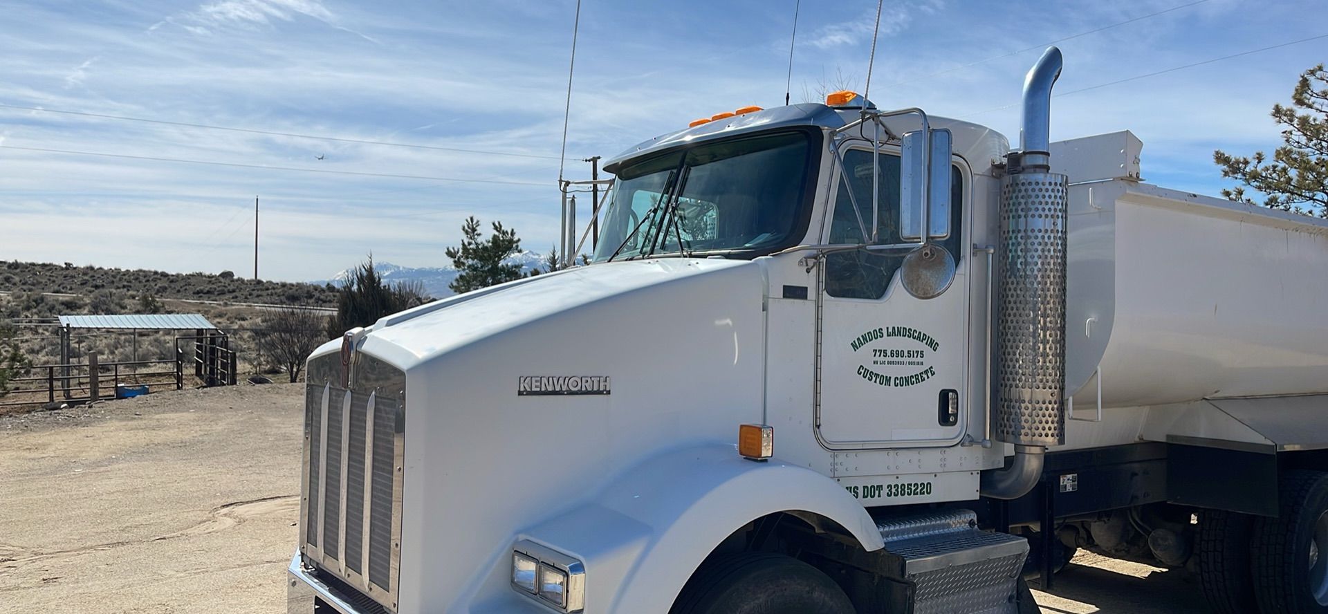 A white dump truck is parked in a dirt field.