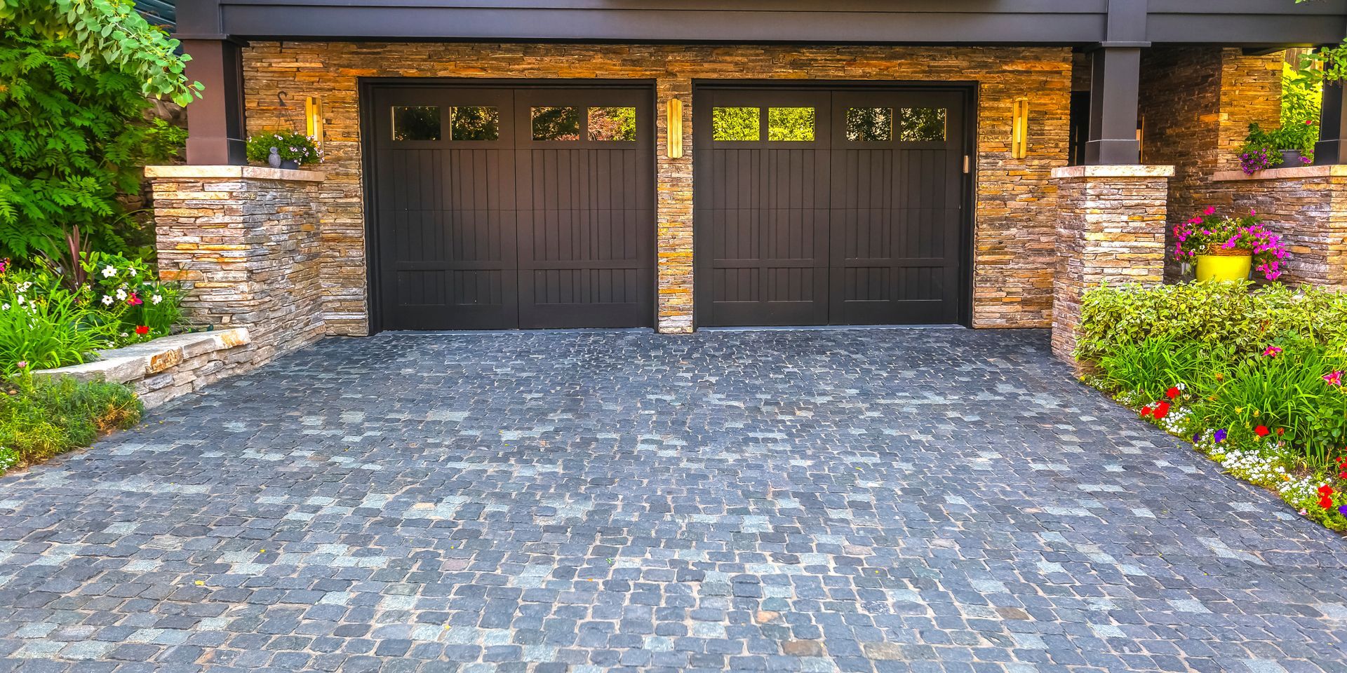 A brick driveway leading to a garage with two black garage doors.