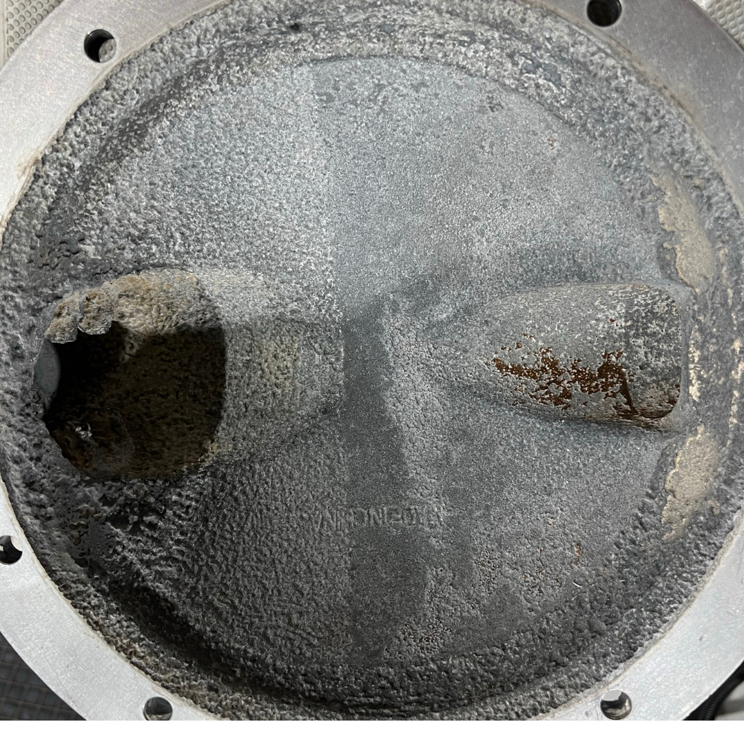 Close-up of a metal component with a worn, textured surface. There is a hole and some discoloration.