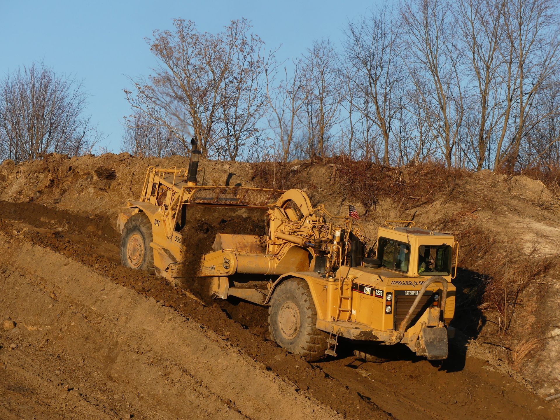 Yellow earthmover working on a dirt embankment under a clear blue sky.
