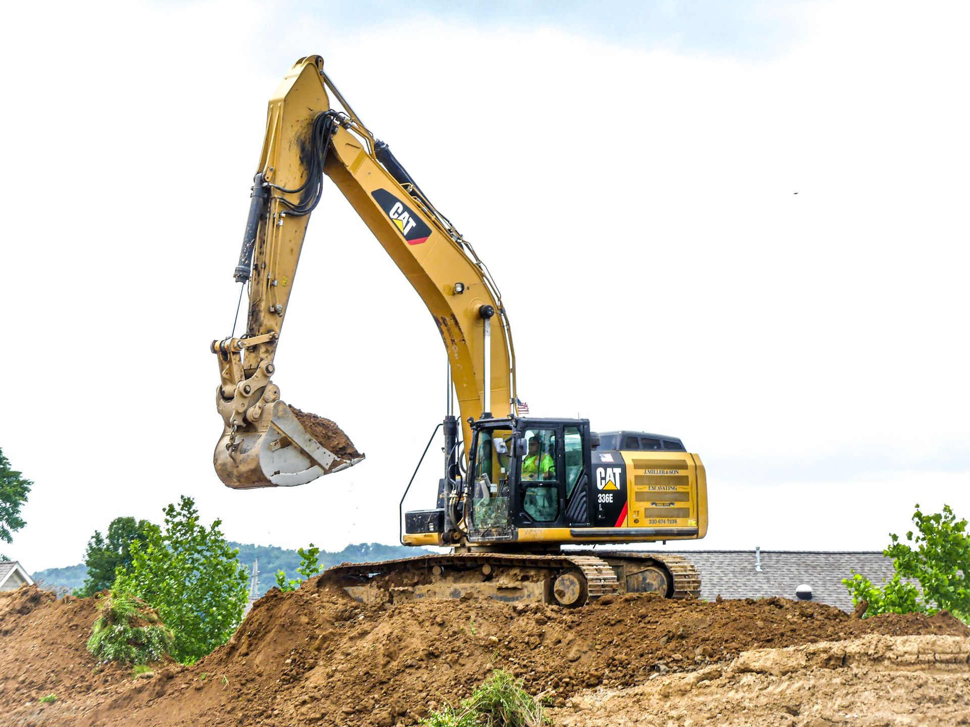 Yellow Caterpillar excavator on a dirt mound, scooping dirt; cloudy sky background.