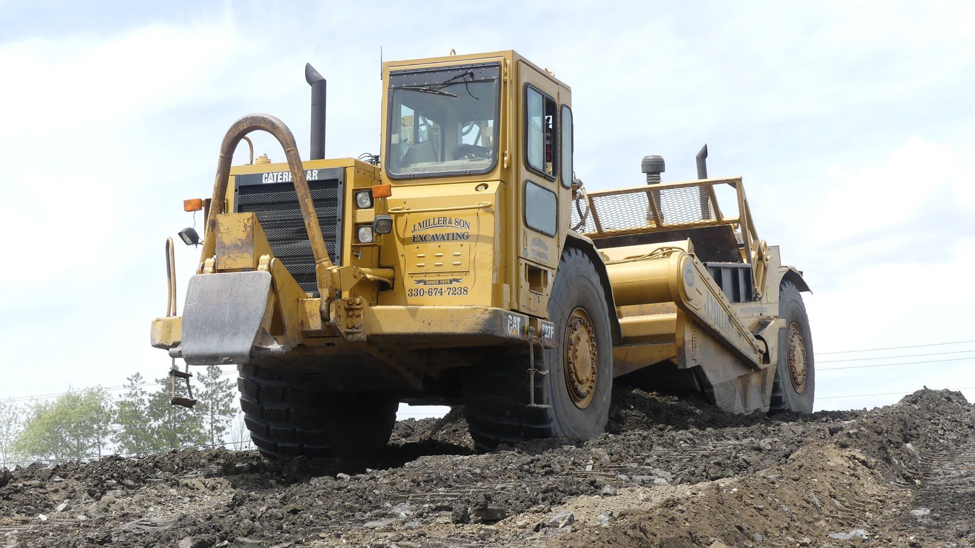 Yellow earth scraper tractor moving soil outdoors.