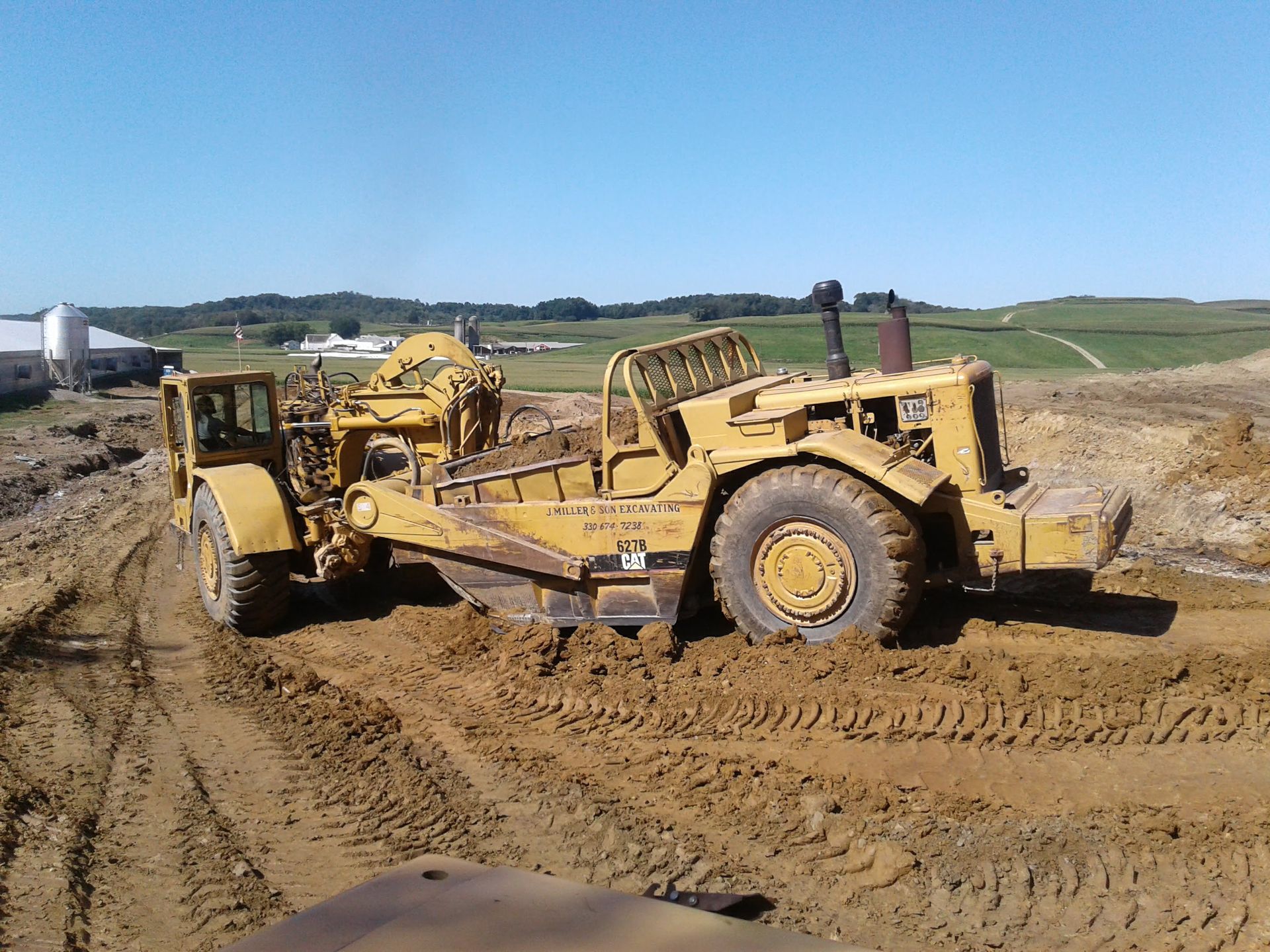 Yellow earth scraper stuck in mud on a construction site.