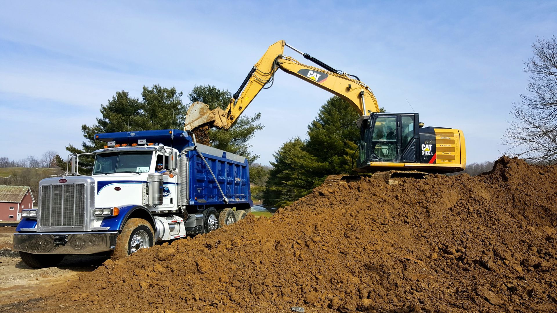 Excavator loading dirt into a blue dump truck outdoors on a sunny day.