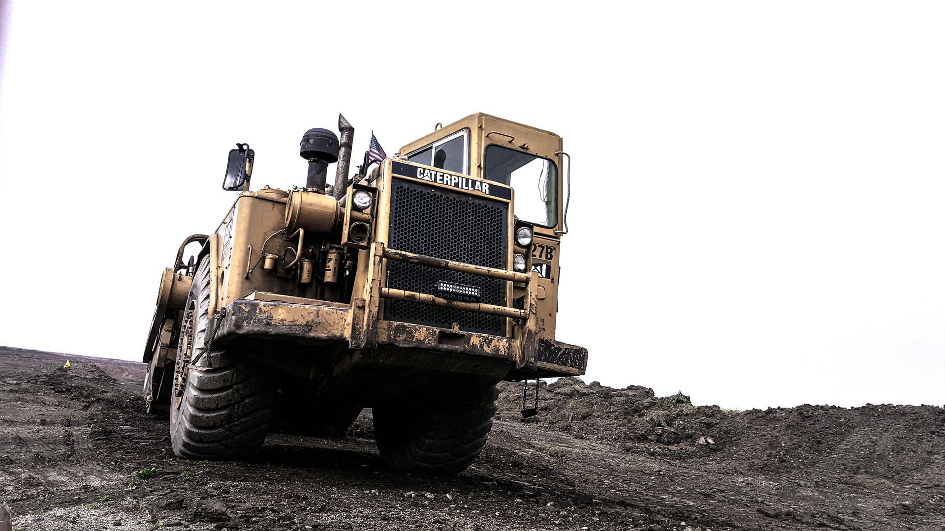 Yellow heavy-duty construction vehicle on a rocky hill against a white sky.