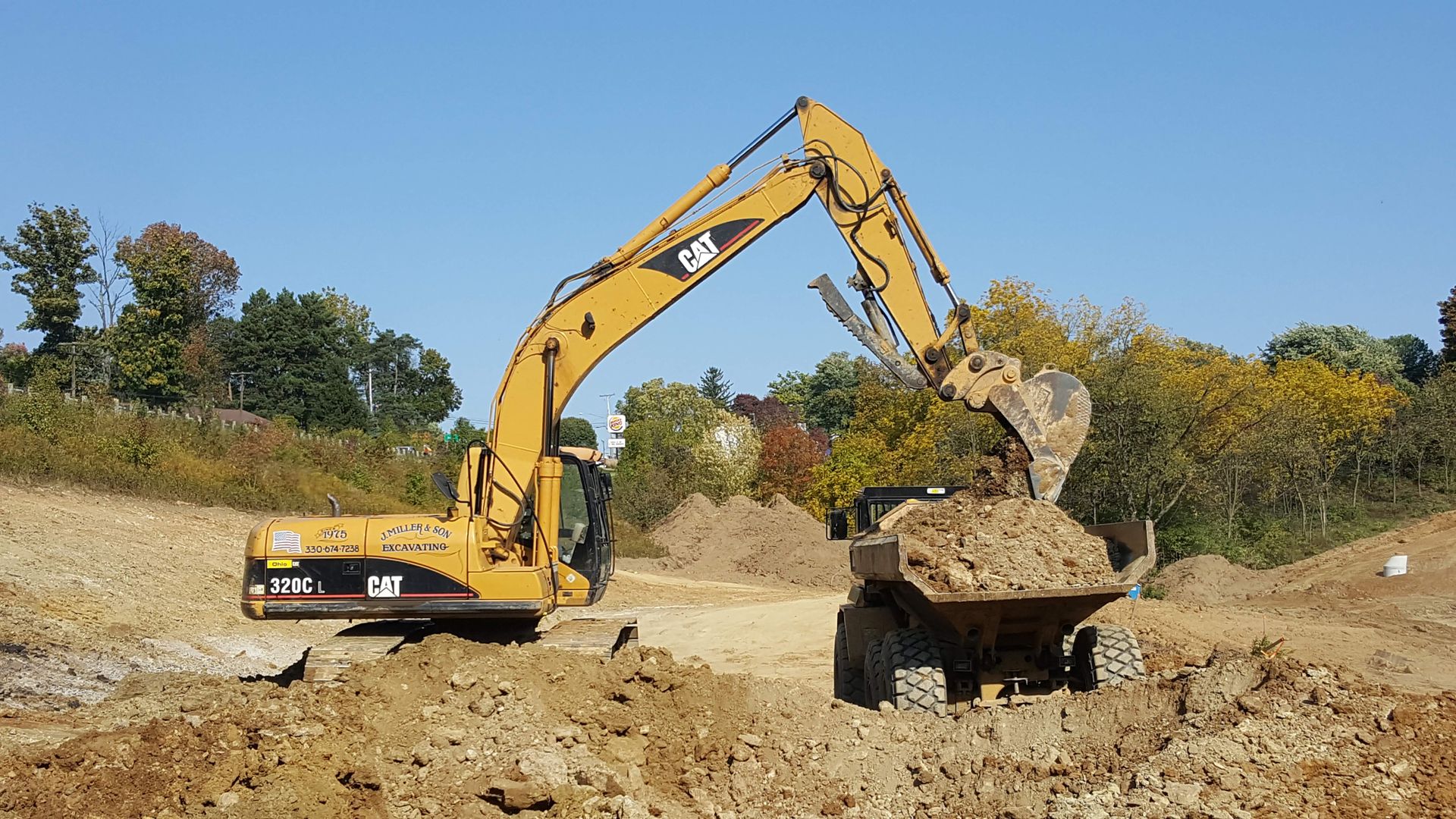 Yellow excavator loading dirt into a dump truck on a construction site.