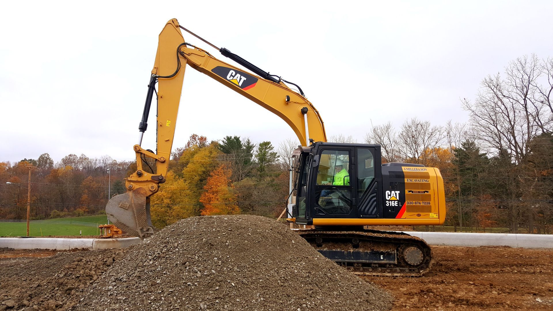 Yellow Caterpillar excavator scoops gravel on a construction site.