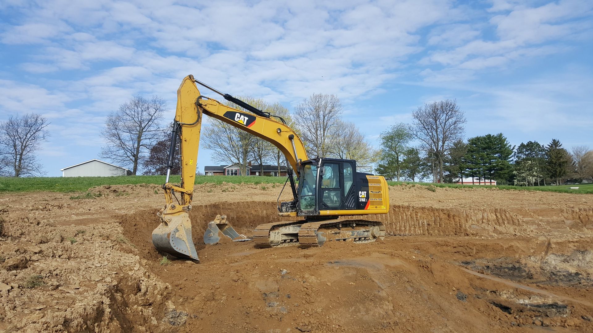 Yellow excavator digging into brown earth on a construction site; blue sky in background.