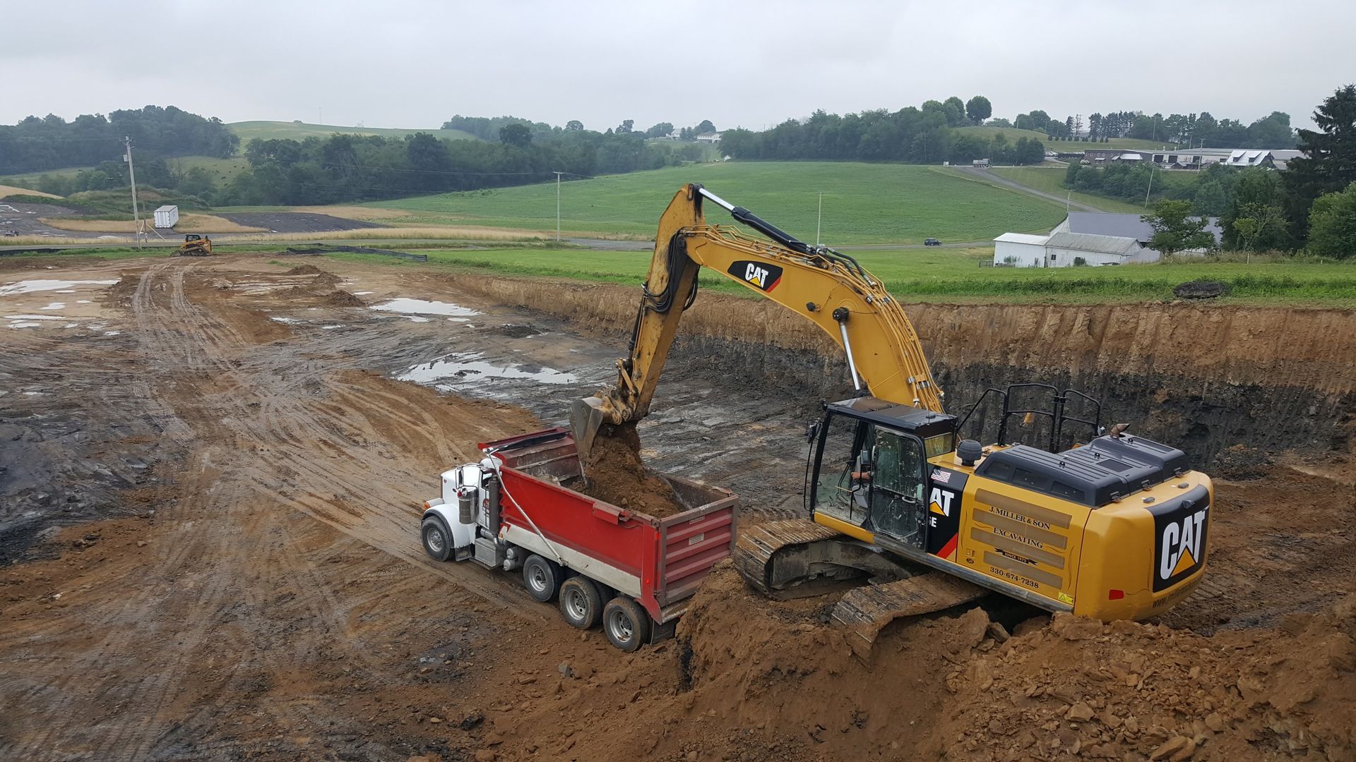 Yellow excavator loading red dump truck with mud at construction site.