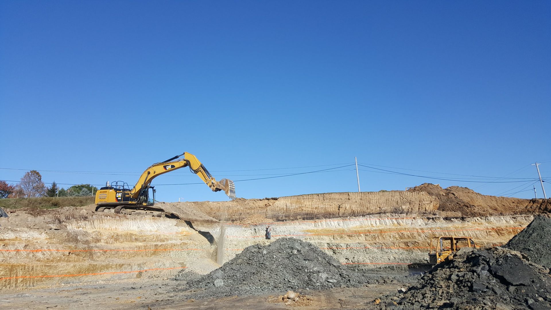 Yellow excavator digging into a layered earth bank under a clear blue sky.