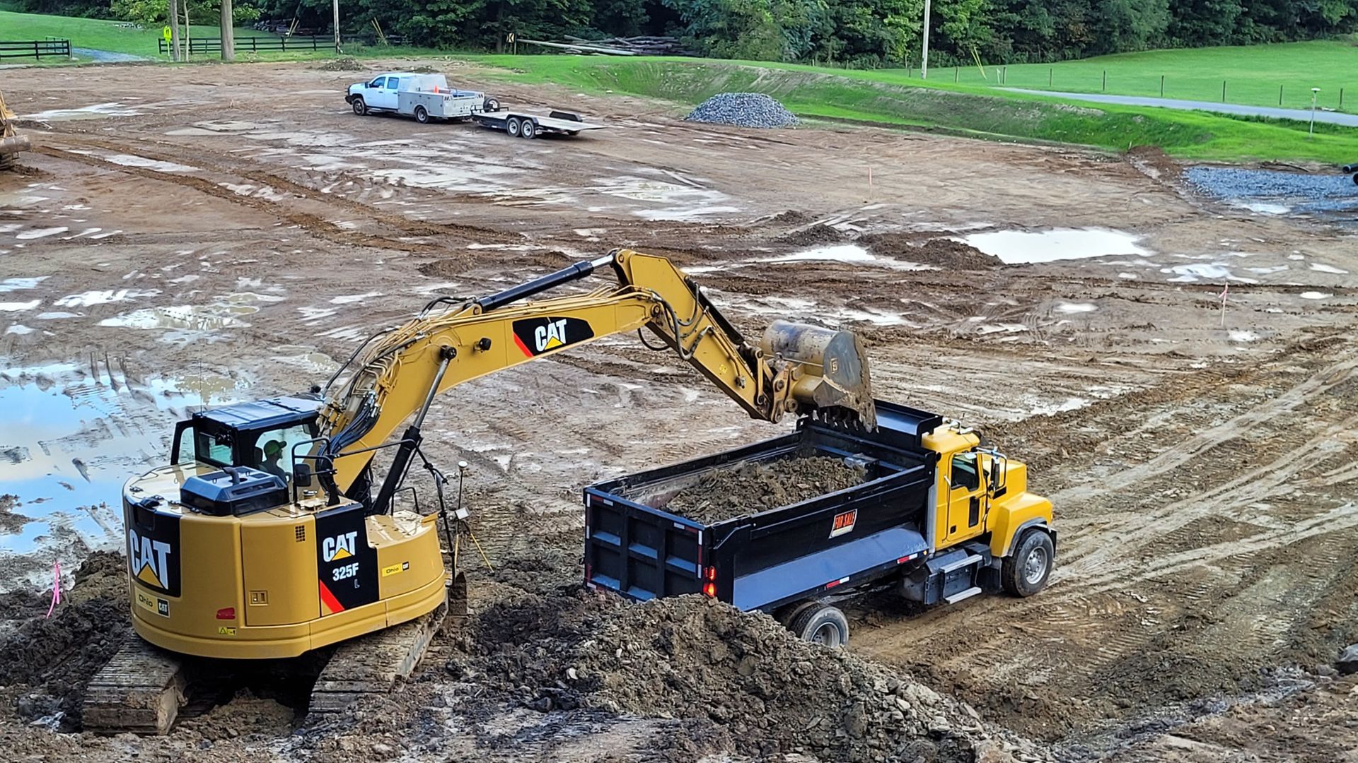 An excavator loading a yellow dump truck with soil at a construction site.