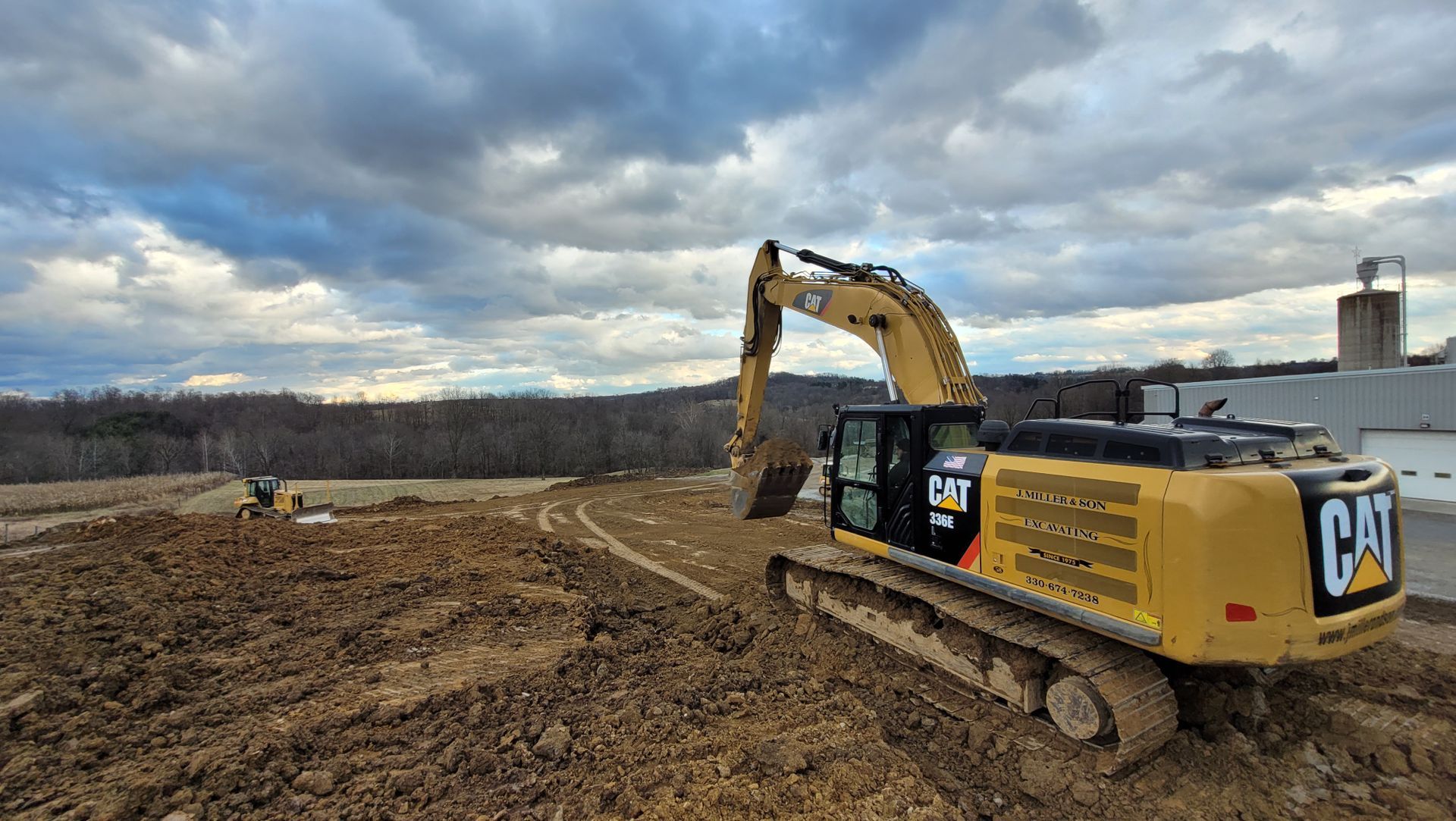 Yellow Caterpillar excavator digging in a dirt field under a cloudy sky.