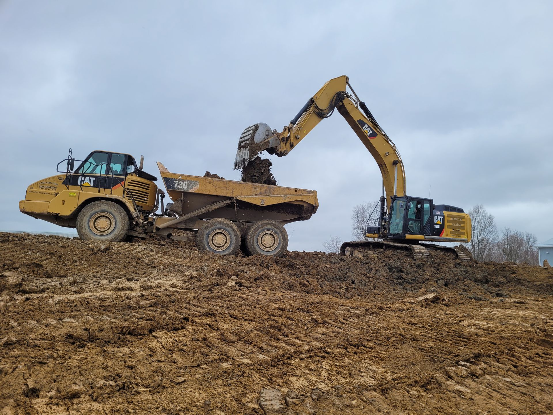 An excavator loading a dump truck with dirt at a construction site on a cloudy day.