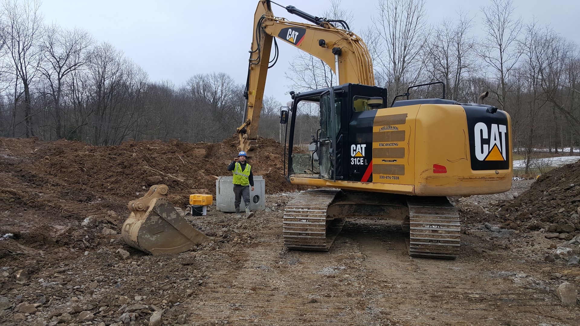 Yellow Caterpillar excavator at construction site, with worker in safety vest.