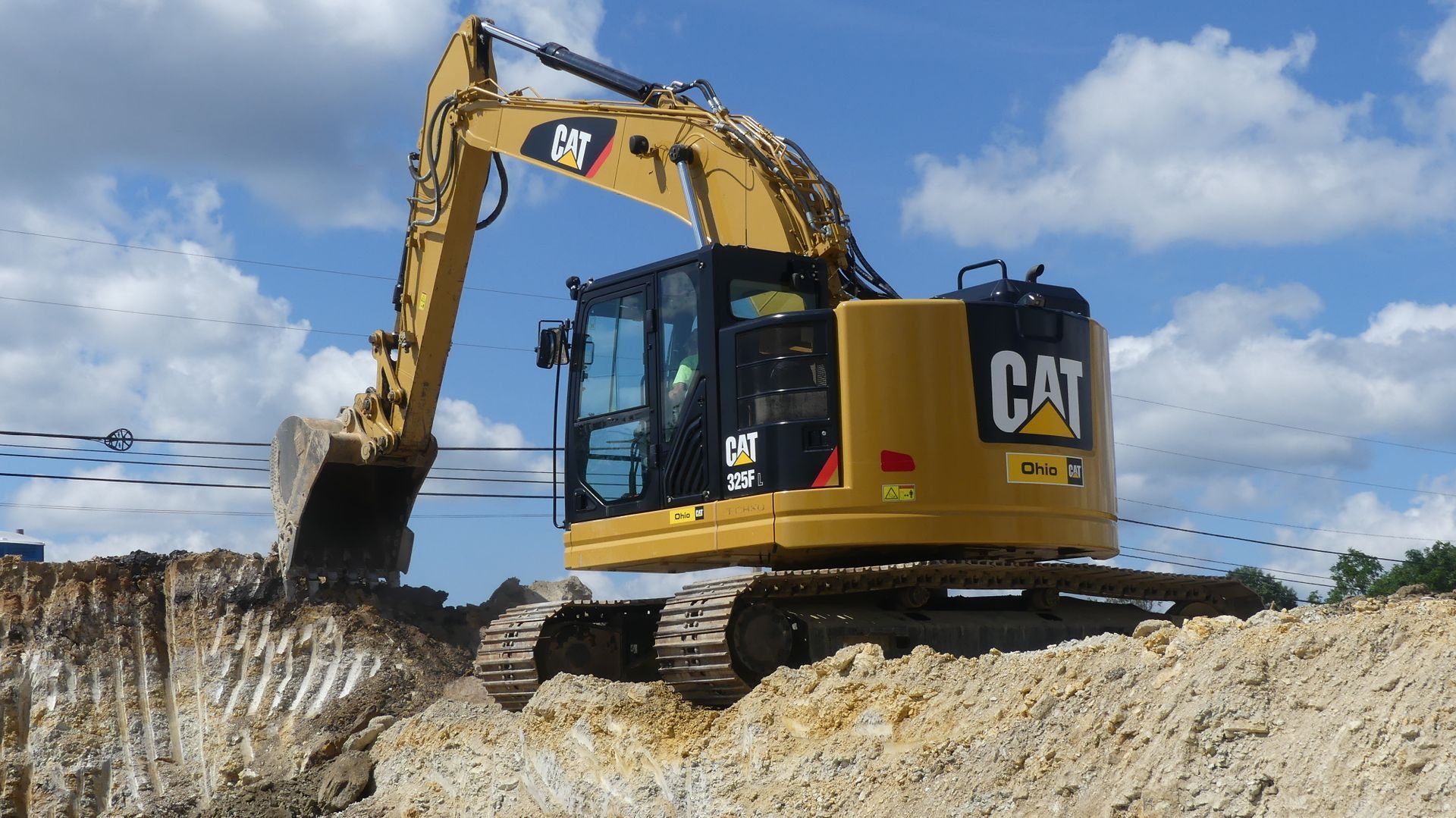 Yellow Caterpillar excavator digging in a dirt pile, under a cloudy sky.