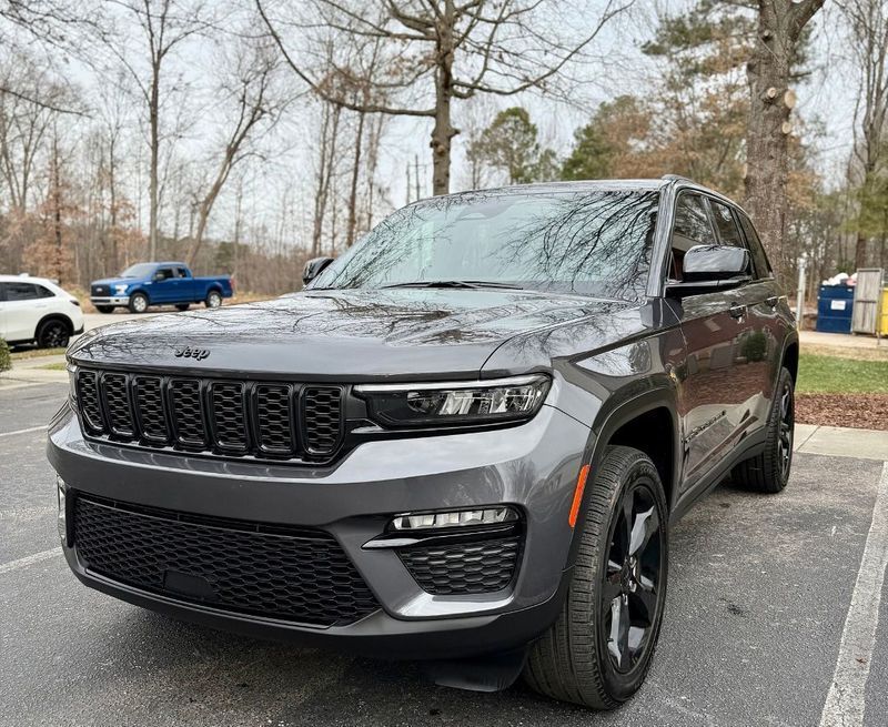 A gray Jeep Grand Cherokee parked in an outdoor lot on a cloudy day, with a blue pickup truck visible in the background.