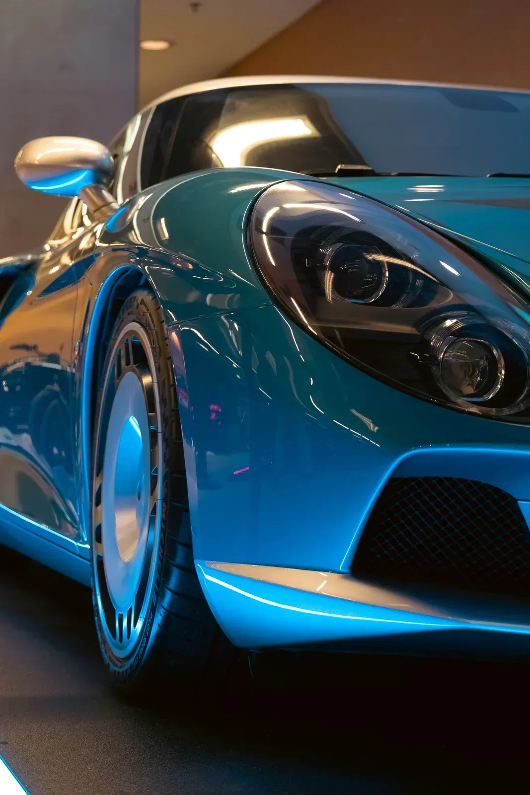 A sleek, teal-colored sports car with a reflective hood and distinct silver wheel rims, viewed from a low front angle.