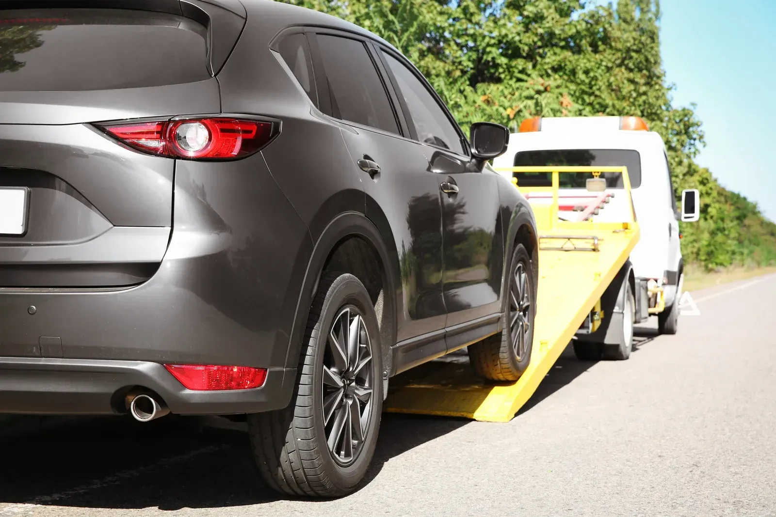 A dark gray SUV being loaded onto the flatbed of a yellow tow truck on a paved road.