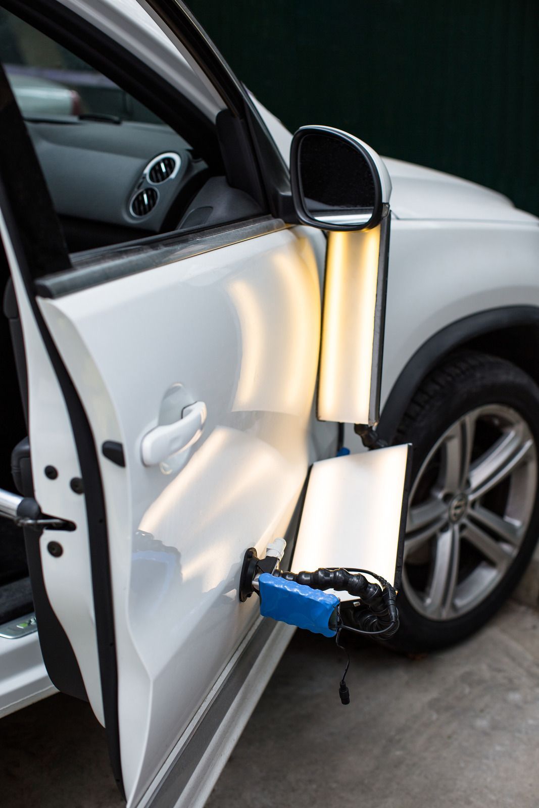 A specialized LED light board is suctioned to the side of a white car to aid in paintless dent repair.
