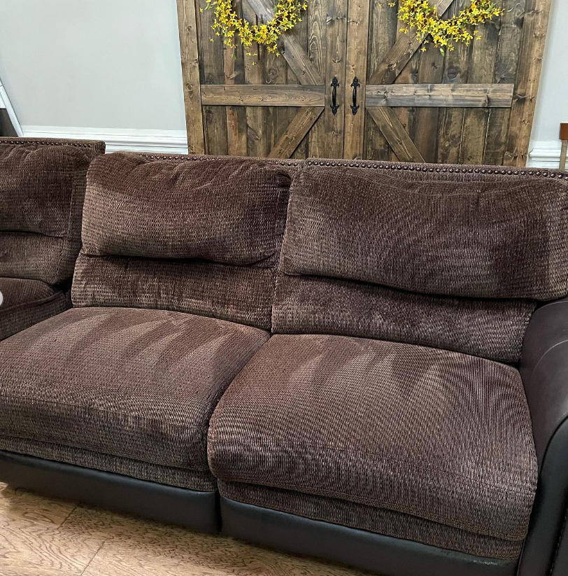 a brown couch is sitting in front of a wooden door in a living room .