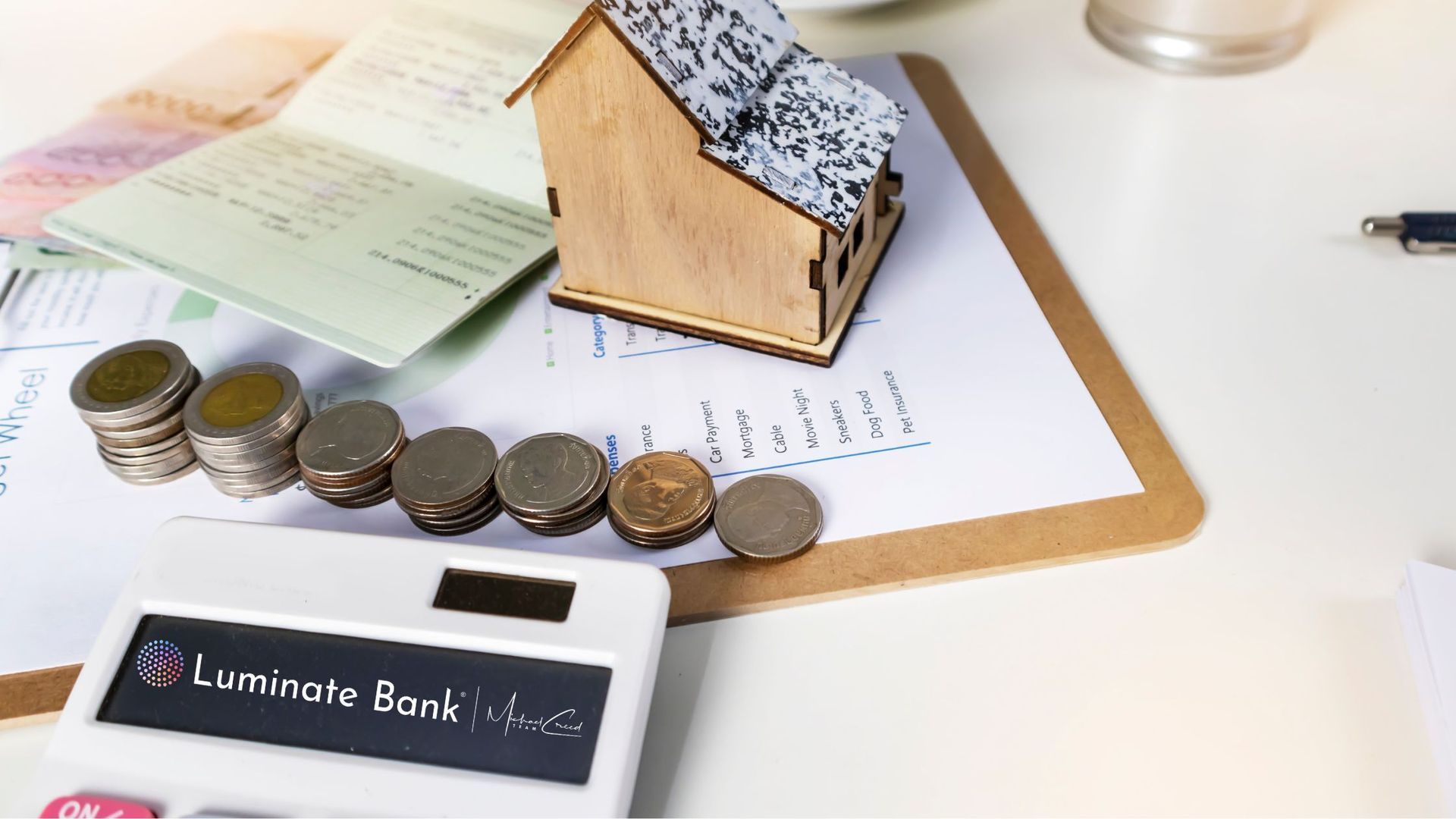 Financial scene: toy house, coins, calculator, bank book, and documents on a desk.