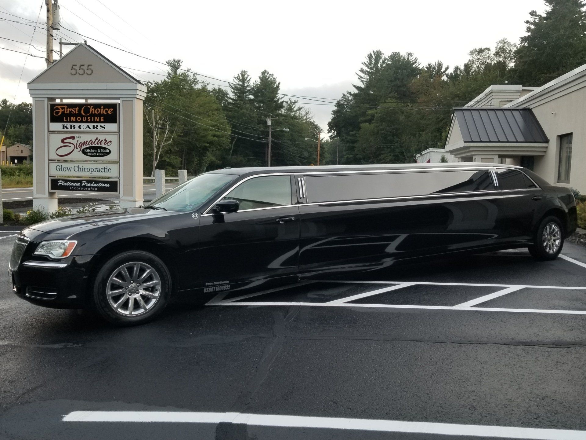 Black limousine parked in front of a building with signs. Cloudy sky.