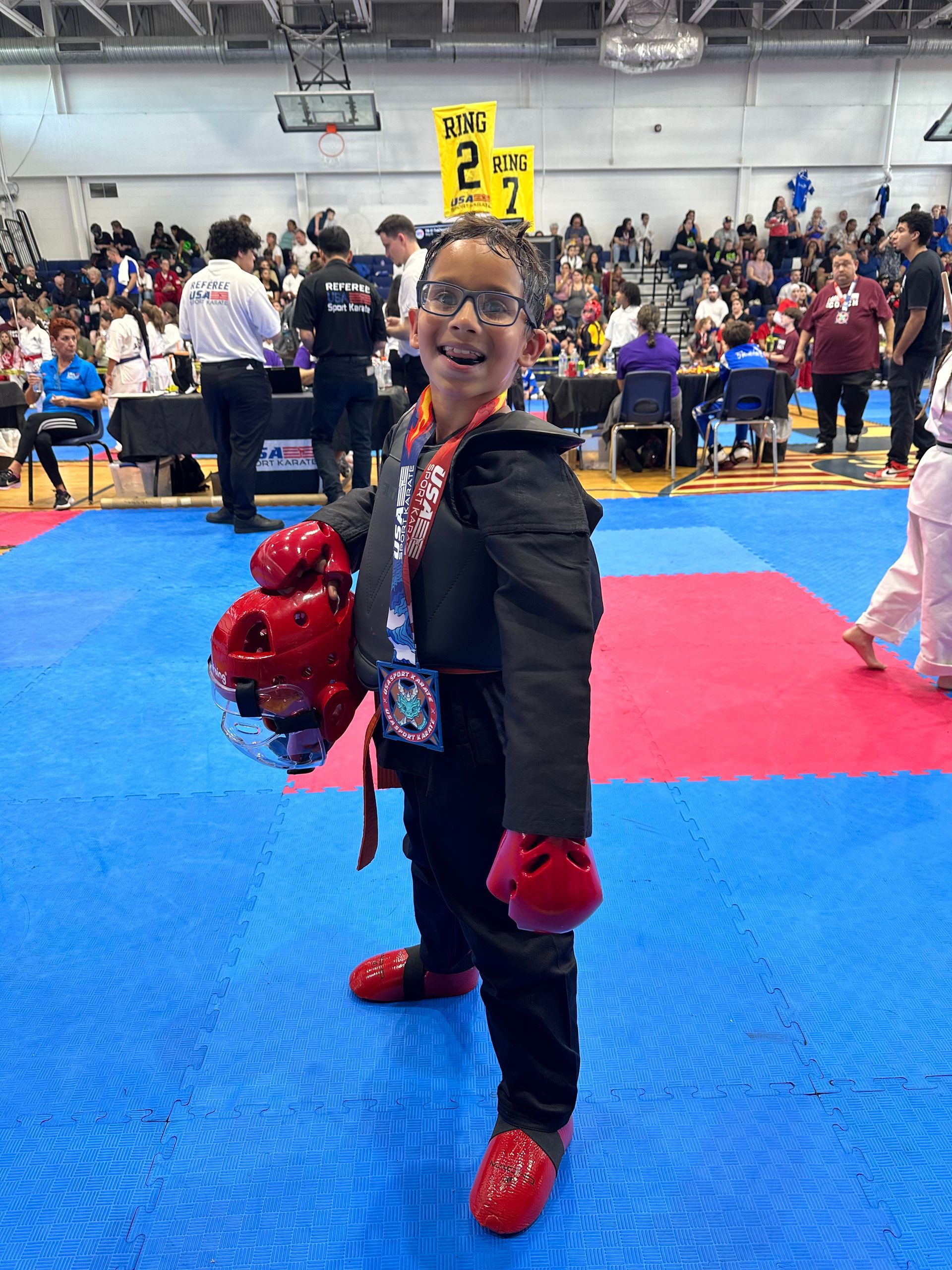 A young boy is standing on a karate mat holding a medal.