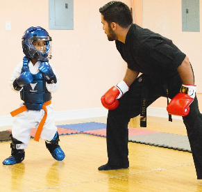 A man wearing boxing gloves stands next to a young boy wearing a helmet