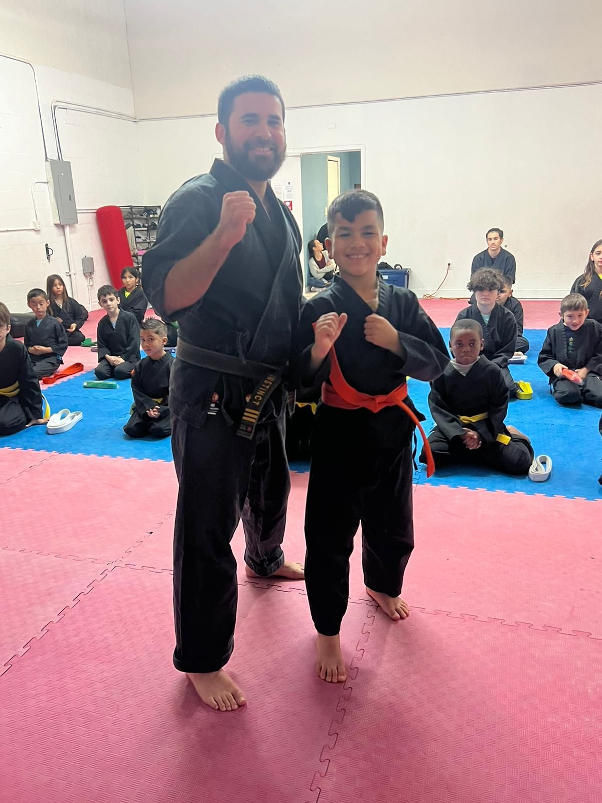 A man and a boy are standing next to each other in a karate class.