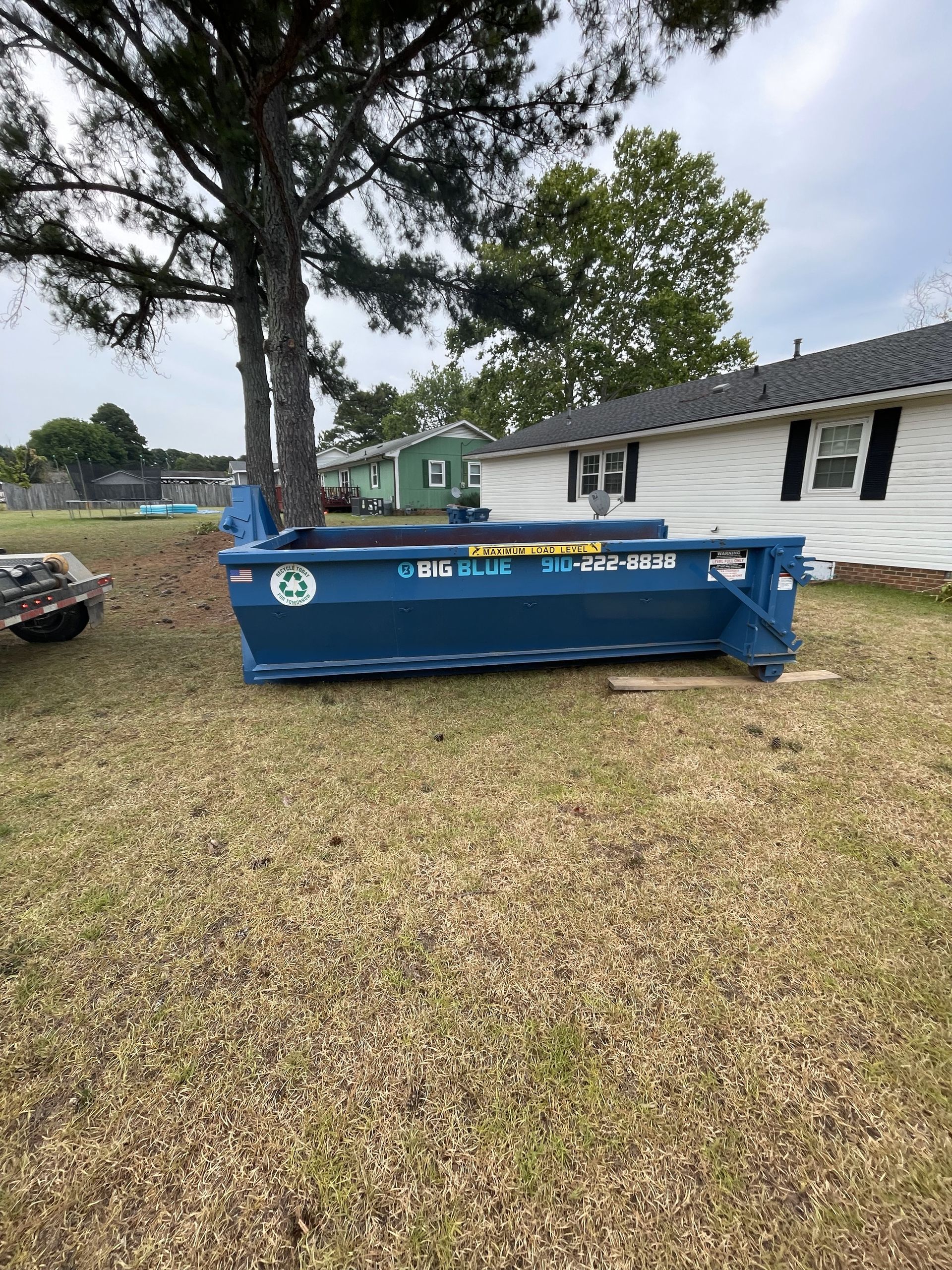 A blue dumpster is sitting in the grass in front of a house.