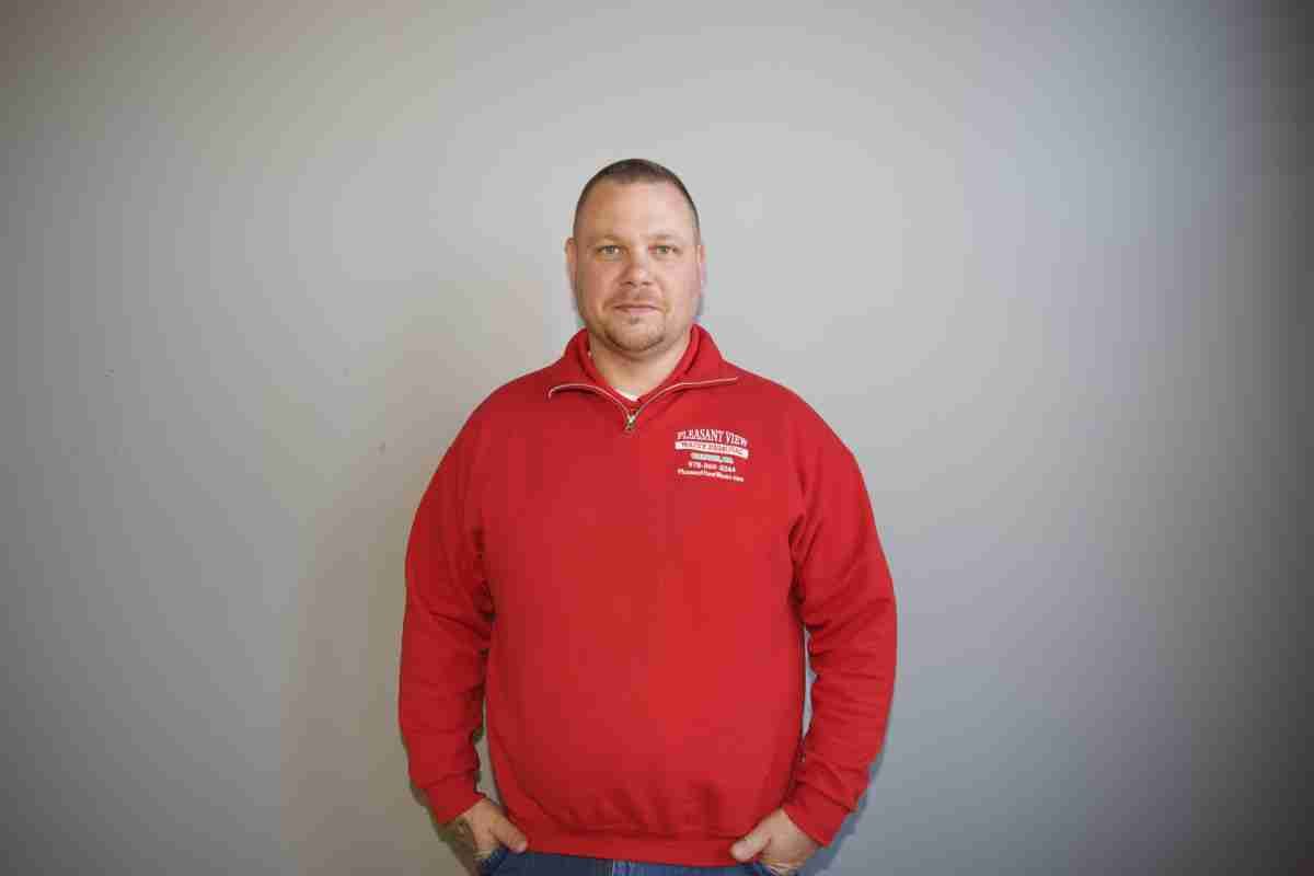 A man in a red sweatshirt is standing with his hands in his pockets.