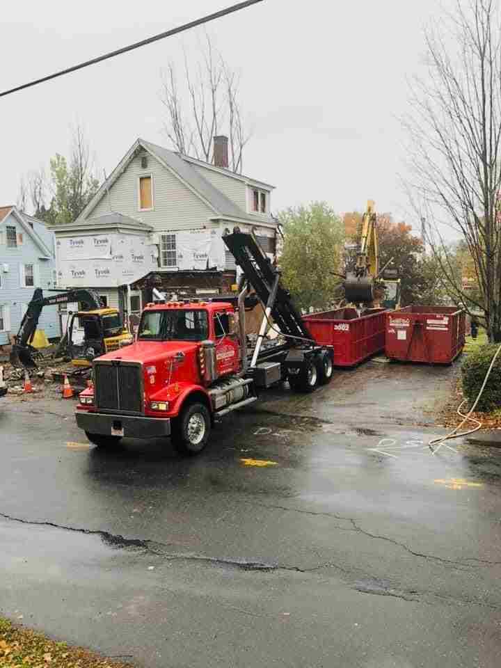 A red dump truck is driving down a street next to a house. A red dump truck is driving down a street next to a house.