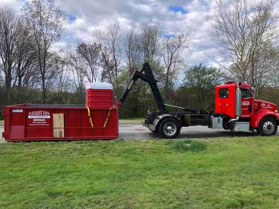 A red dump truck is pulling a red dumpster in a grassy field.