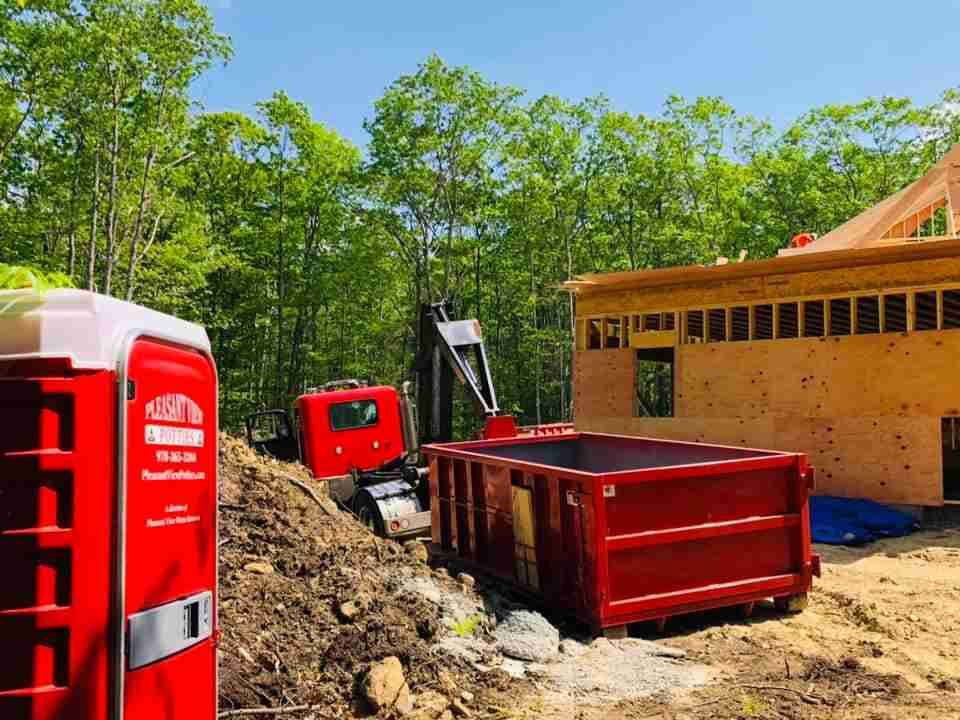 A red dumpster is sitting in front of a house under construction.