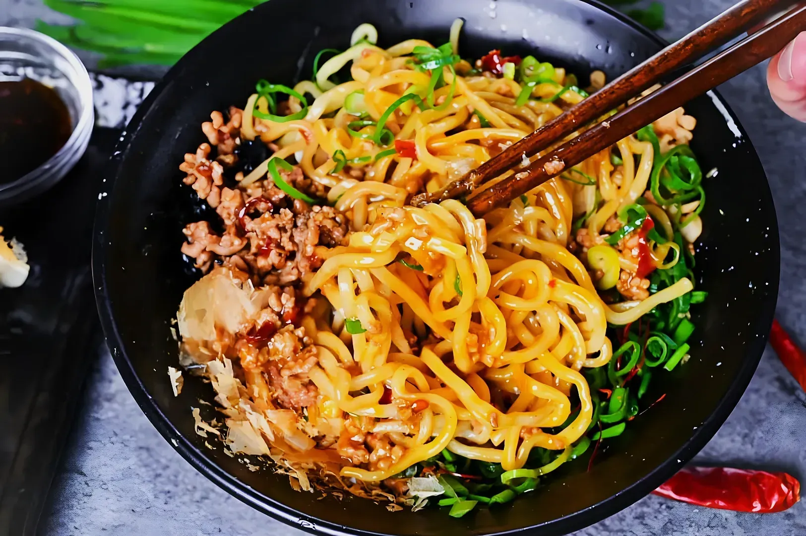A bowl of spicy noodles topped with minced meat, scallions, and chili slices.