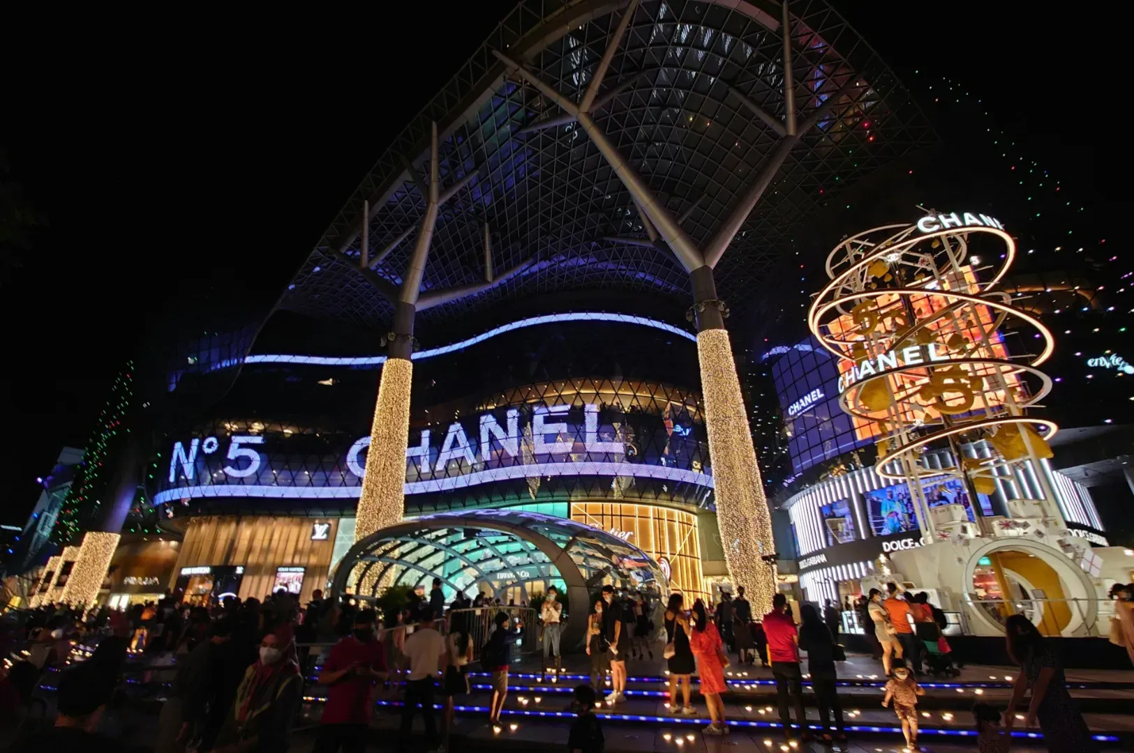 Illuminated luxury shopping center at night with prominent Chanel signage.