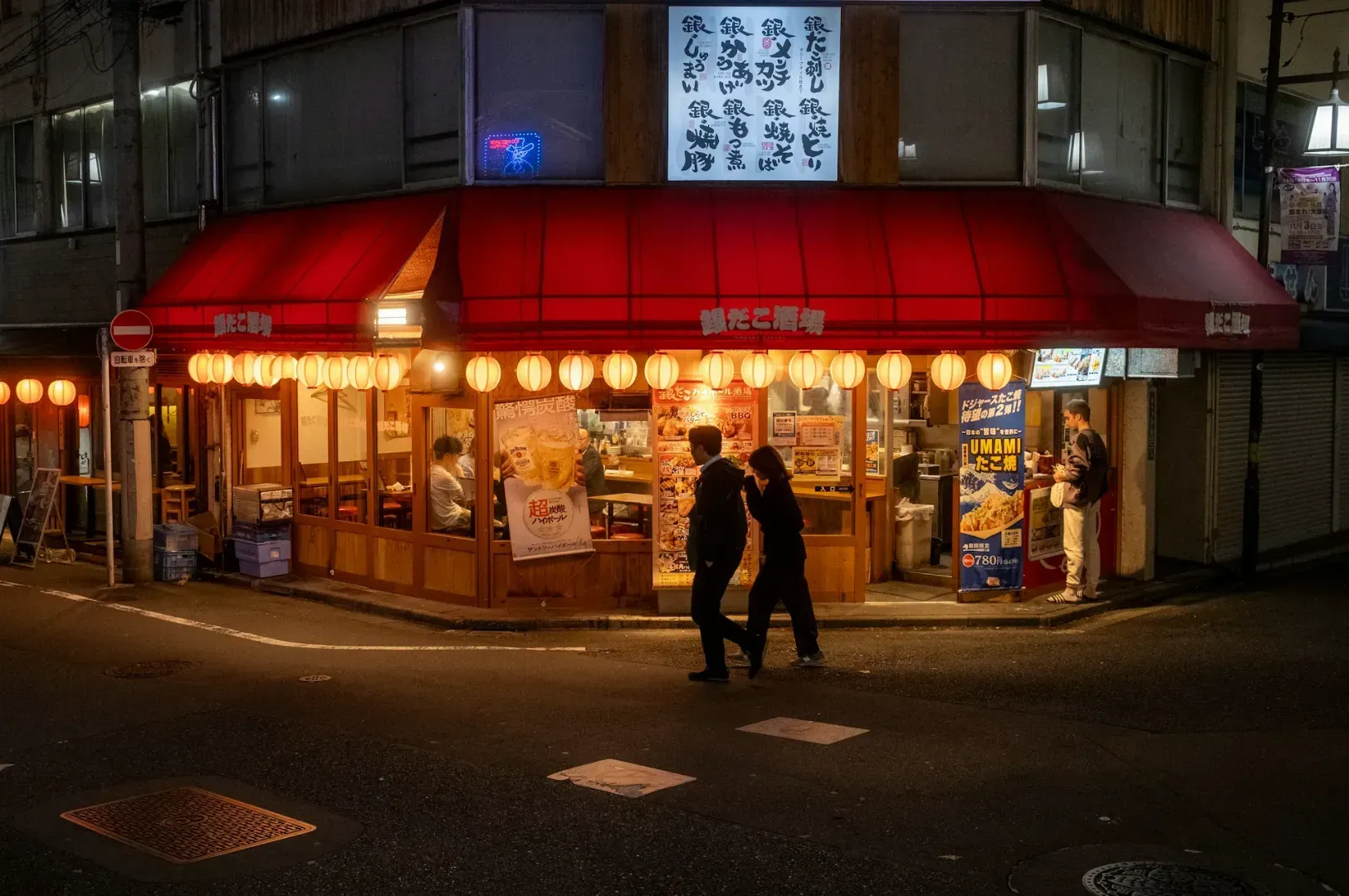 A cozy, warmly lit Japanese restaurant on a corner street at night.