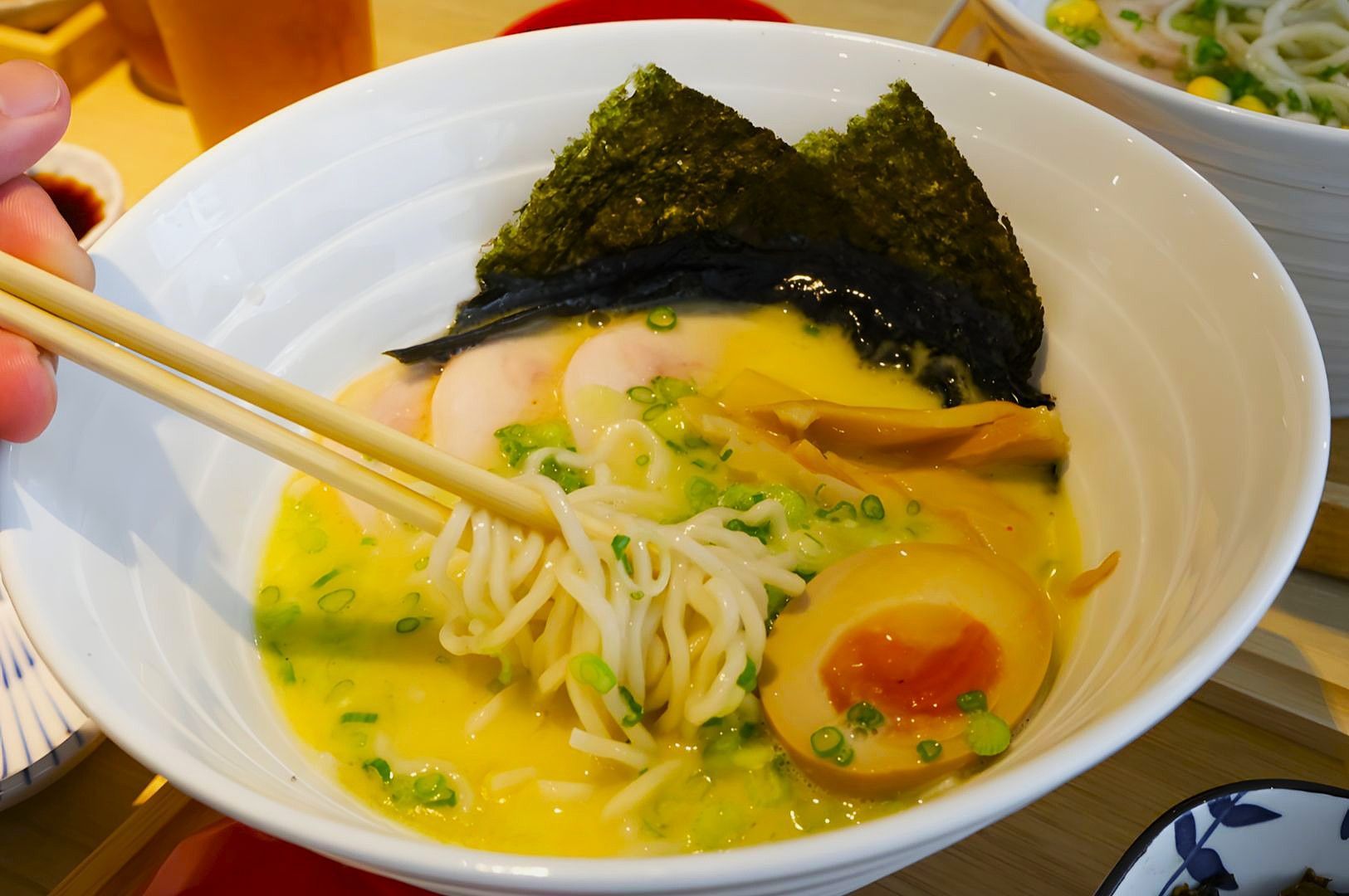 A bowl of ramen with creamy broth, topped with seaweed, sliced egg, bamboo shoots, and green onions.