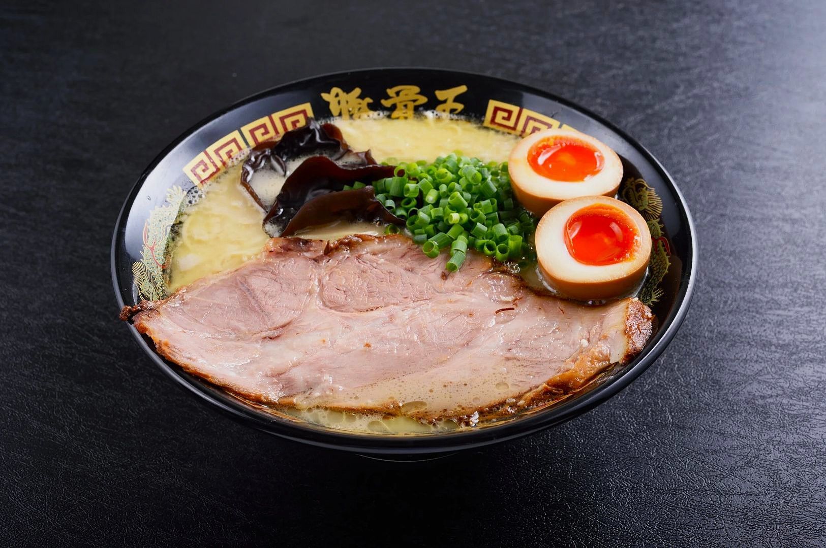 A black bowl of ramen with sliced pork, vibrant soft-boiled eggs, green onions, and mushrooms.