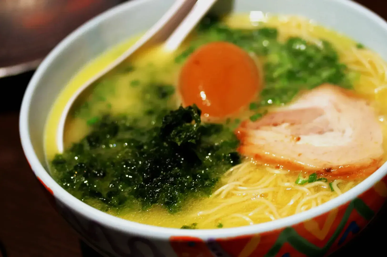 A close-up of a steaming bowl of ramen with creamy broth, topped with sliced pork, a soft-boiled egg