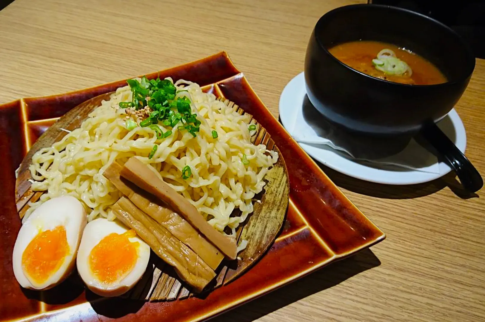 A plate of chilled ramen noodles garnished with green onions, bamboo shoots, and soft-boiled eggs.