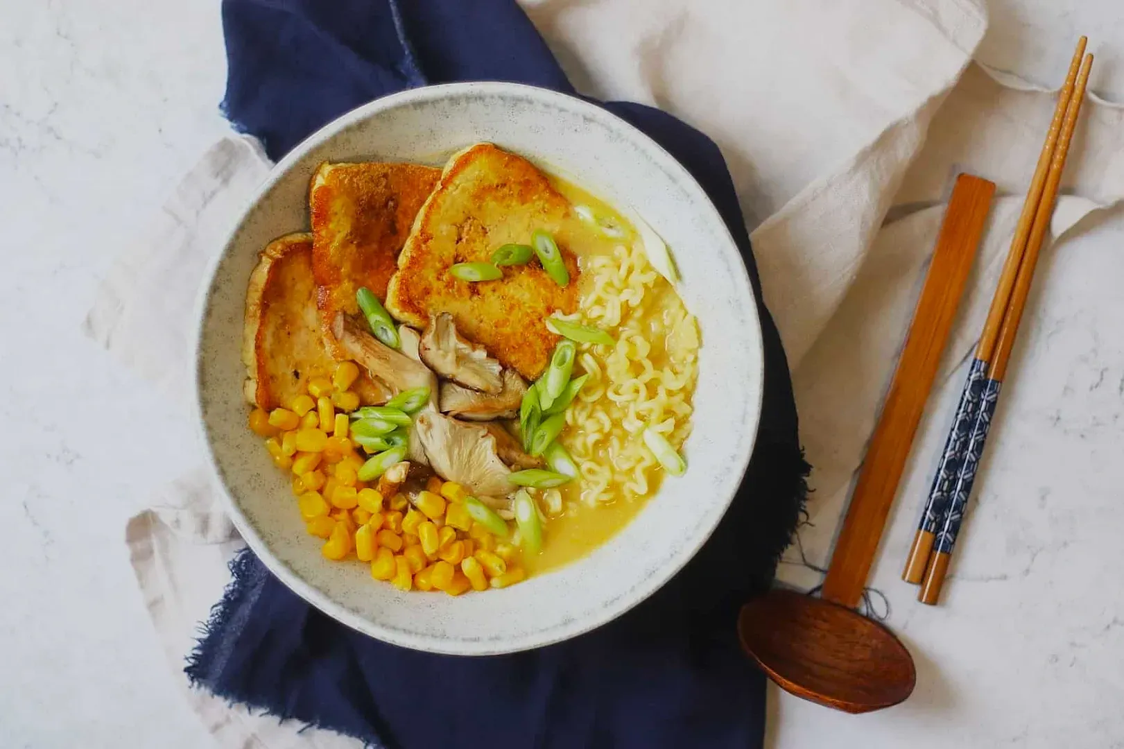 A bowl of ramen with creamy broth, topped with seared tofu, corn, mushrooms, and green onions.