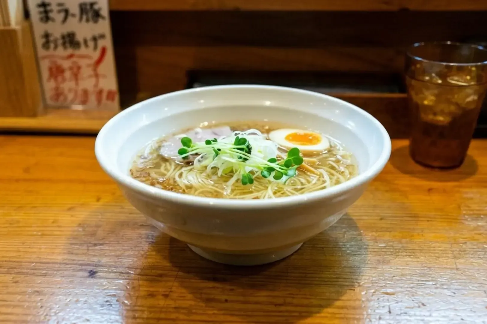 Clear yuzu shio ramen bowl with noodles, soft-boiled egg, microgreens, and pork slice.