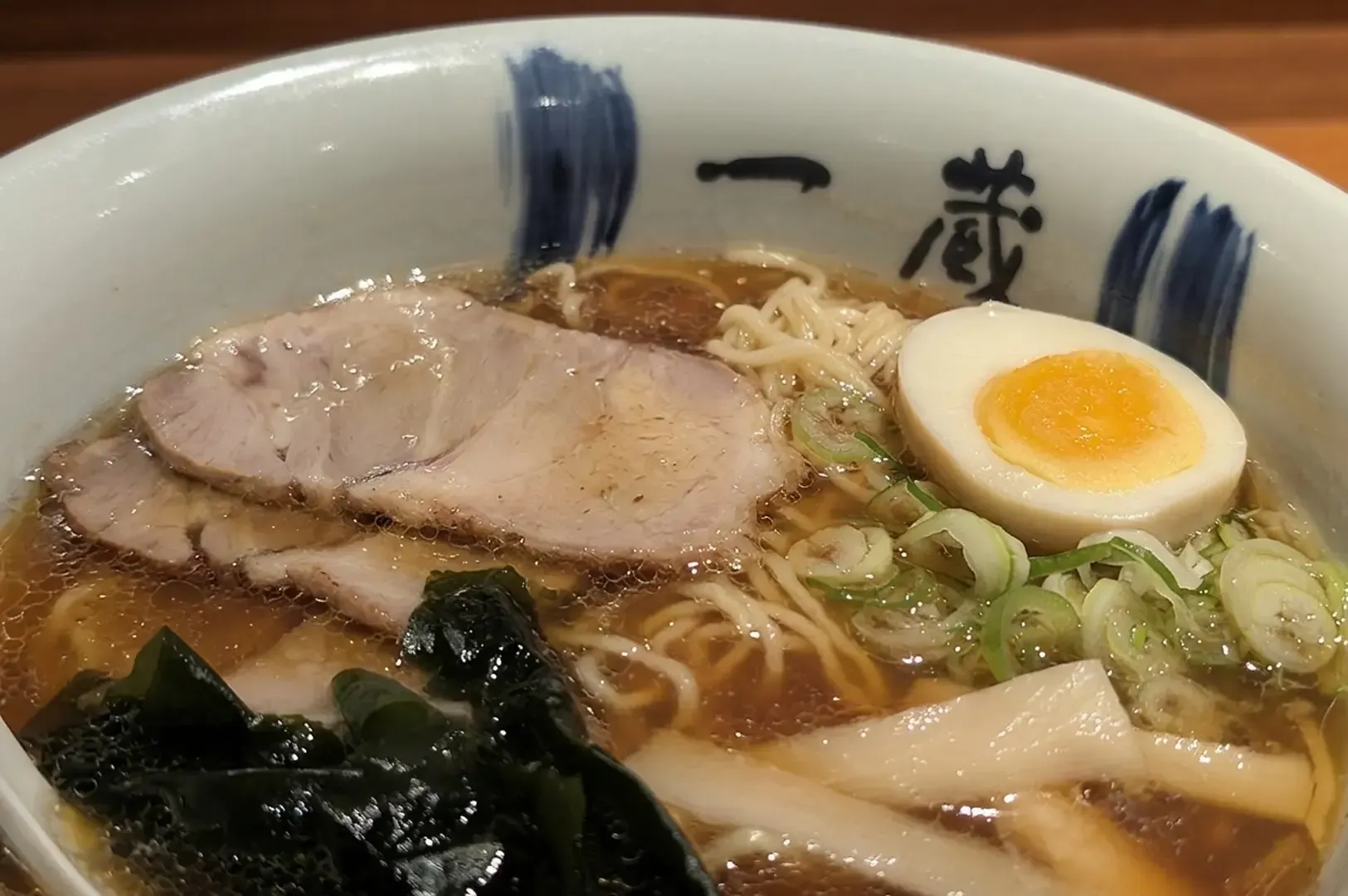 Asahikawa shoyu ramen bowl with chashu pork slices, soft-boiled egg, green onions, seaweed.