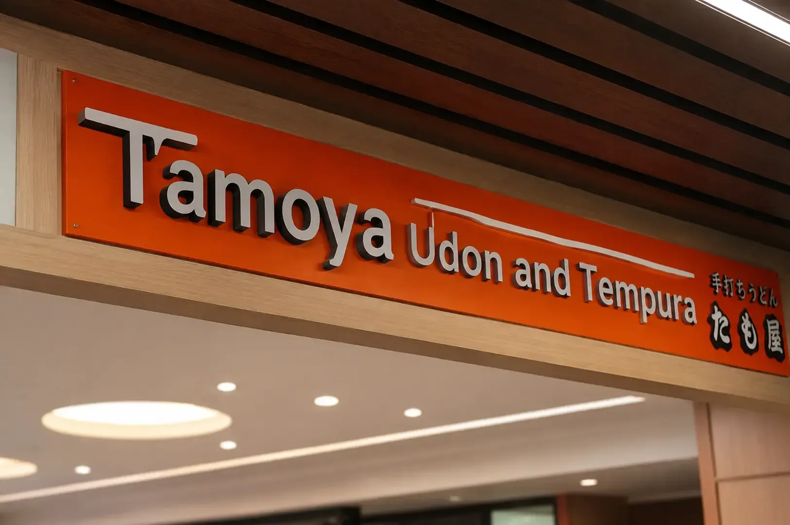 Close-up of the bright orange Tamoya Udon and Tempura signboard with white lettering and Japanese.