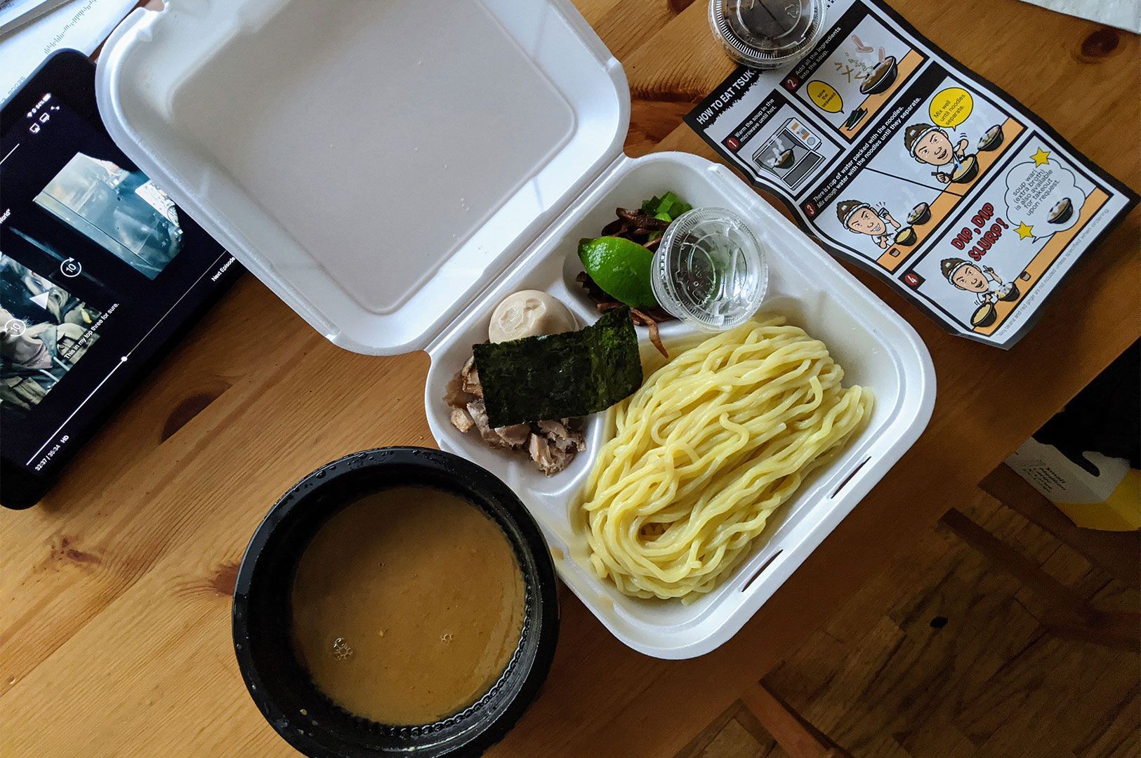 Overhead view of a Japanese tsukemen ramen takeout kit in a white styrofoam container with noodles.